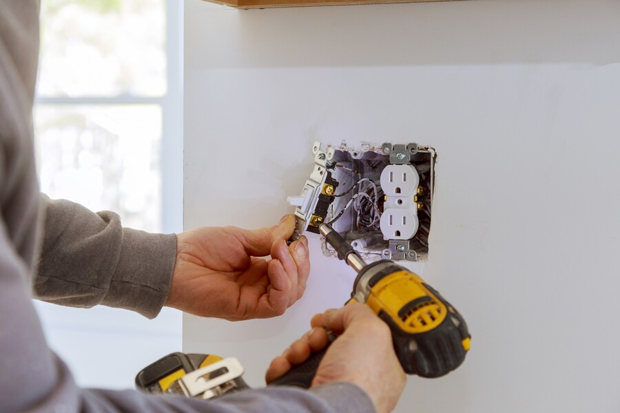 Electrician installing a wall switch and outlet with a drill during home electrical repair