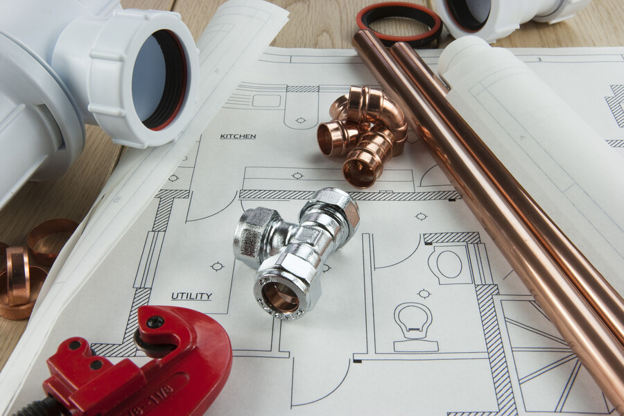 Plumbing pipes, fittings, and tools laid out on a house blueprint for kitchen and utility areas
